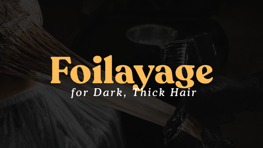 Close-up of a stylist applying lightener with a brush to a section of dark hair in foils, with the bold text “Foilayage for Dark, Thick Hair” overlaid in orange and white.